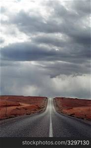 A straight desert road under stormy sky; vertical frame; Maroc, Africa.