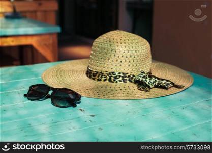 A straw hat and a pair of sunglasses on a table in the sunlight