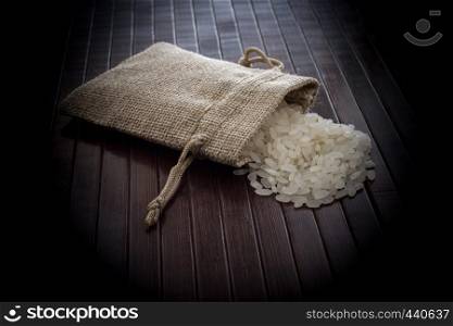 A straw pouch full of uncooked rice on a wooden background