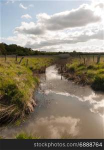 a stream running through the country with clouds reflected in it