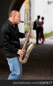 A street musician playing his saxophone serenades two young lovers