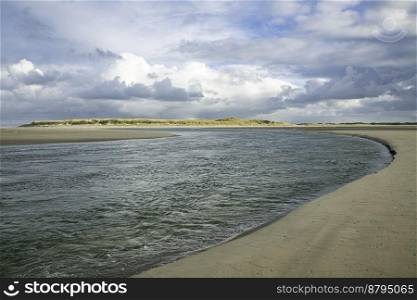 a stretch of beach by the sea with the sun on the du≠s in the background of the island of Texel in the Netherlands. dark clouds over the sea with sunshi≠on the du≠s≠ar the beach