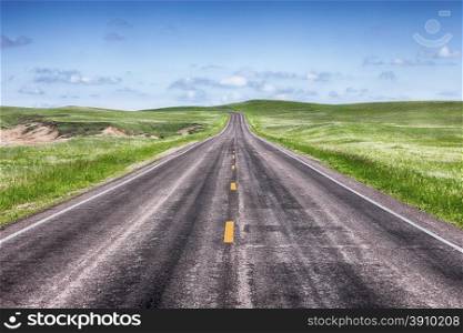 A stretch of straight road in the prairie grasslands of Badlands National Park in South Dakota turns at the horizon to go over the hills.