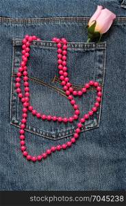 A string of pink beads and a pink artificial rose displayed in the back pocket of a denim jean