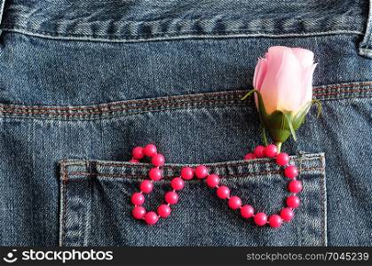 A string of pink beads and a pink artificial rose displayed in the back pocket of a denim jean