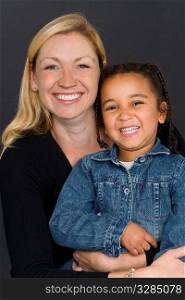 A studio shot of a happy smiling beautiful young mixed race little girl and a caucasian woman in her thirties