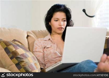 A stunningly beautiful young Hispanic woman sitting on a settee using her laptop