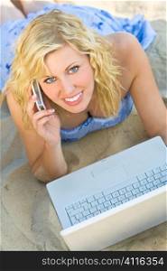 A stunningly beautiful young woman using her laptop and cell phone at the beach