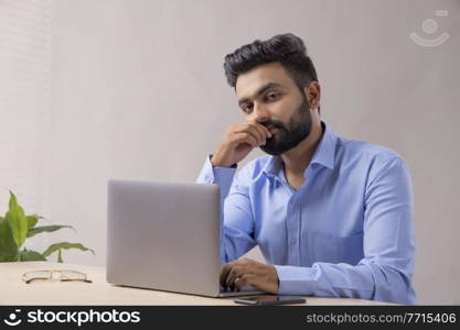 A STYLISH BEARDED MAN LOOKING AT CAMERA WHILE WORKING