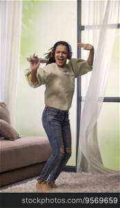 A STYLISH YOUNG WOMAN HAPPILY DANCING WHILE LISTENING TO MUSIC AT HOME