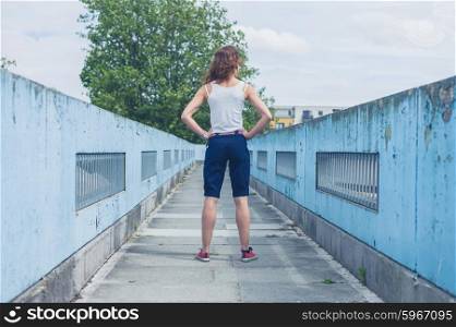 A stylish young woman is standing on a footbridge