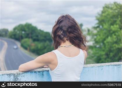 A stylish young woman is standing on a footbridge