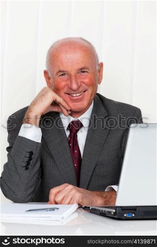a successful older businessman sits in his office with a laptop.