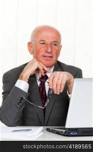 a successful older businessman sits in his office with a laptop.