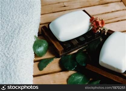 A super close up of a hard soap over a soap dish with relaxing spa style with a towel and plants