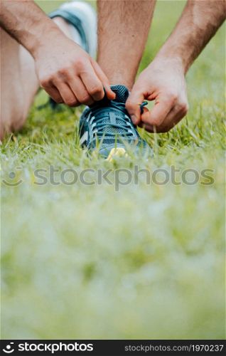 A super close up of a man tying the shoelaces on this sport shoes over green grass before training fitness