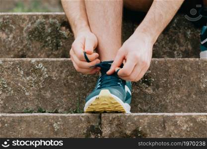 A super close up of a man tying the shoelaces on this sport shoes over concrete before training fitness