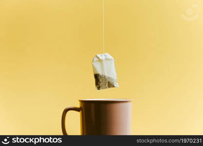 A super minimalistic shot of a bag of fast tea over a pink cup over a pastel yellow background