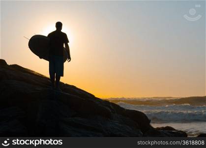 A surfer watching the waves at sunset in Portugal.