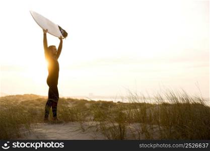 A surfer with his surfboard at the dunes looking to the waves