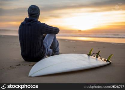 A surfer with his surfboard at the sunset looking to the waves