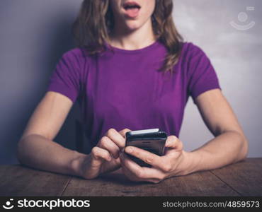 A surprised young woman is using a smartphone at a table