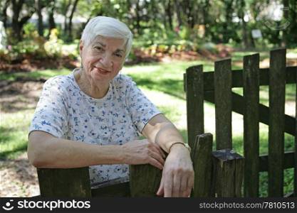 A sweet senior lady leaning on her garden gate.