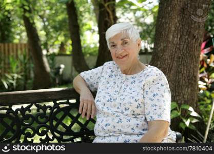 A sweet senior lady relaxing on a park bench. Room for text.