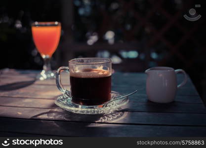 A table in the sunlight with a cup of coffee and a glass of juice