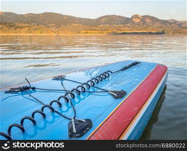 A tail of stand up paddleboard with a leash and bungees on a mountain lake (Horsetooth Reservoir), late summer morning