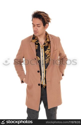 A tall young handsome man standing with his hands in his coat pocket looking down, isolated for white background