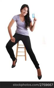 A tall young woman, sitting on a chair and holding her first credit card inher hand, with long brunette hair and black jeans, for white background.