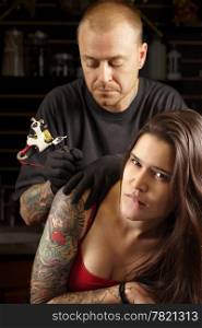 A tattoo artist applying his craft onto the back and arm of a female in her 20&rsquo;s. Focus on female&rsquo;s face (Property release for tattoo artwork attached)