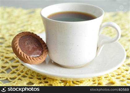 A tea cup with a round biscuit displayed on a crochet cloth