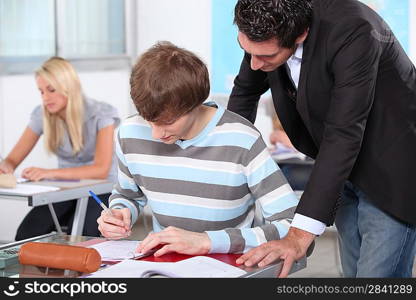 A teacher overlooking the work of one of his pupils in a classroom.