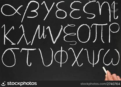 A teacher writing the Greek alphabet on a blackboard.