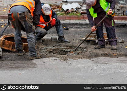 A team of road service workers in reflective vests are repairing a sewer hatch on the roadway. Copy space.. Road service workers change the sewer hatch on the roadway.