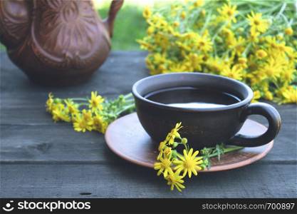 A teapot and a cup of tea stand on wooden blue boards with yellow daisy flowers. Close-up.. A teapot and a cup of tea stand on wooden old boards with yellow daisy flowers. With copy space.