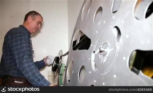 A technician rewinds the a 35mm film reel. 35mm film cinema technical footage. Film Technician mounting a 35mm film reel in a film festival.
