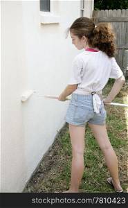 A teen girl rolling paint on an exterior wall of her house.