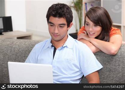 A teenage couple checking their laptop on a couch.