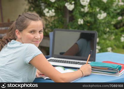 a teenage girl doing her homework with laptop in the garden
