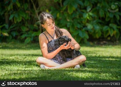A teenage girl plays with her Labrador puppy outside on the lawn of their garden.