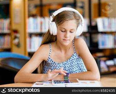 A teenage girl with headphones sitting in a library. Reading and listening