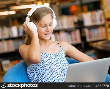 A teenage girl with headphones sitting in a library. Reading and listening