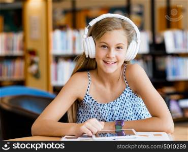 A teenage girl with headphones sitting in a library. Reading and listening