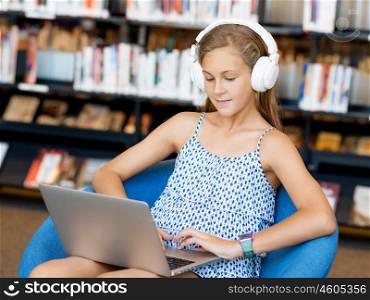 A teenage girl with headphones sitting with a laptop. Browsing with music