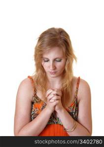 A teenager girl in an orange dress and with blond hair sitting in the studiopraying to God, for white background.