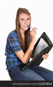 A teenager schoolgirl, with her pen in her mouth, thinking about her homework, in jeans and a chickened blue blouse, over white.