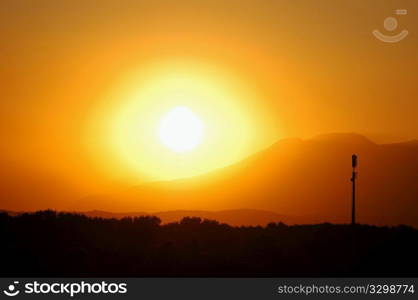 A telcom tower stands against the red sunset sky